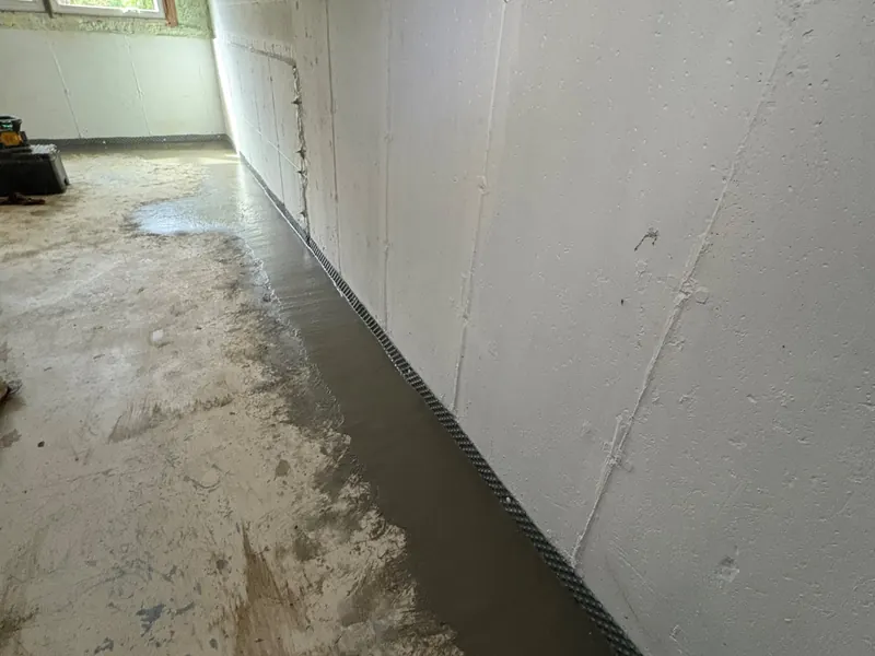 After: a finished basement with water at the base of the wall, then a new interior drain along it