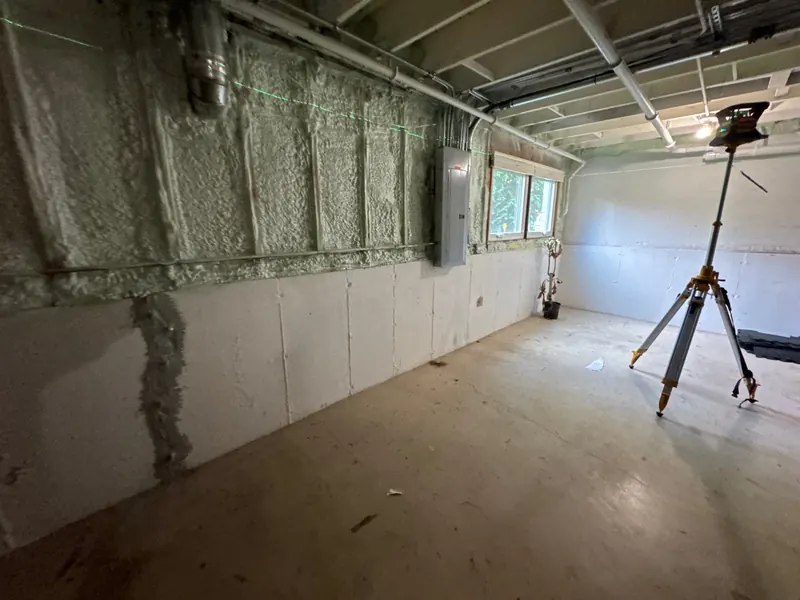 Basement wall with spray foam on the top half and a grey patch lower down.